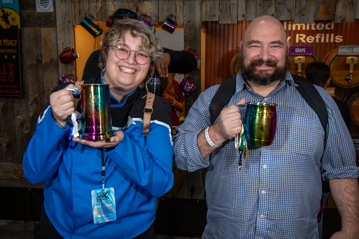 Two smiling fans holding Wild Bill’s mugs at the Wild Bill’s soda wagon